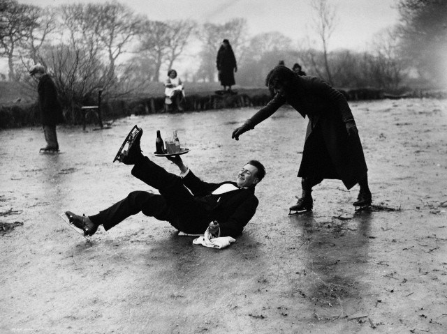 13 Feb 1936, London, England, UK --- An ice skating waiter manages to keep his tray upright after slipping on a frozen pond. His customers include people skating on the pond. Hampstead, London, England, February 13, 1936. --- Image by © Hulton-Deutsch Collection/CORBIS