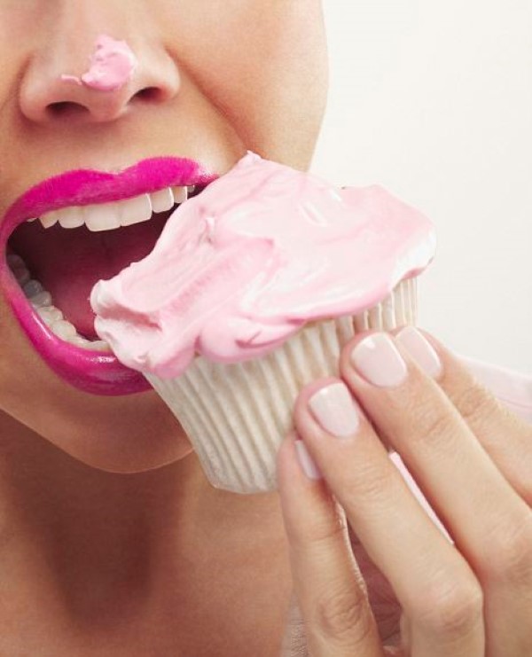 Close up of woman with pink lipstick and frosting on nose eating cupcake